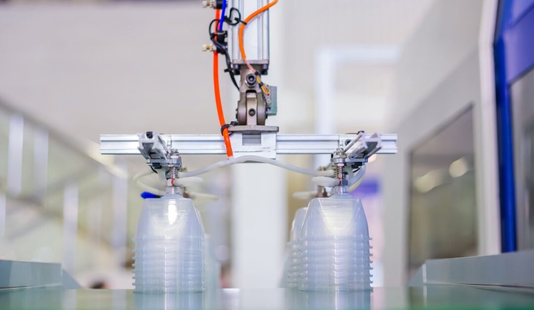 Two stacks of plastic containers on a conveyor belt with a mechanical arm from a plastic molding injection machine overhead.