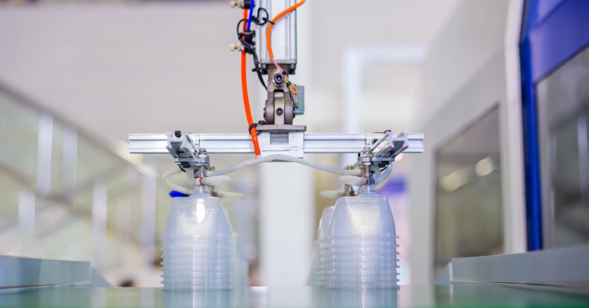 Two stacks of plastic containers on a conveyor belt with a mechanical arm from a plastic molding injection machine overhead.