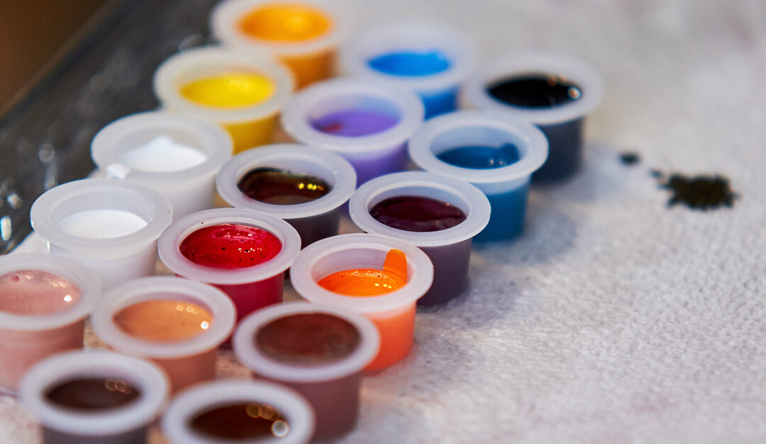 Plastic tattoo ink caps lined in rows on a paper towel. There are different ink colors poured into each cap.