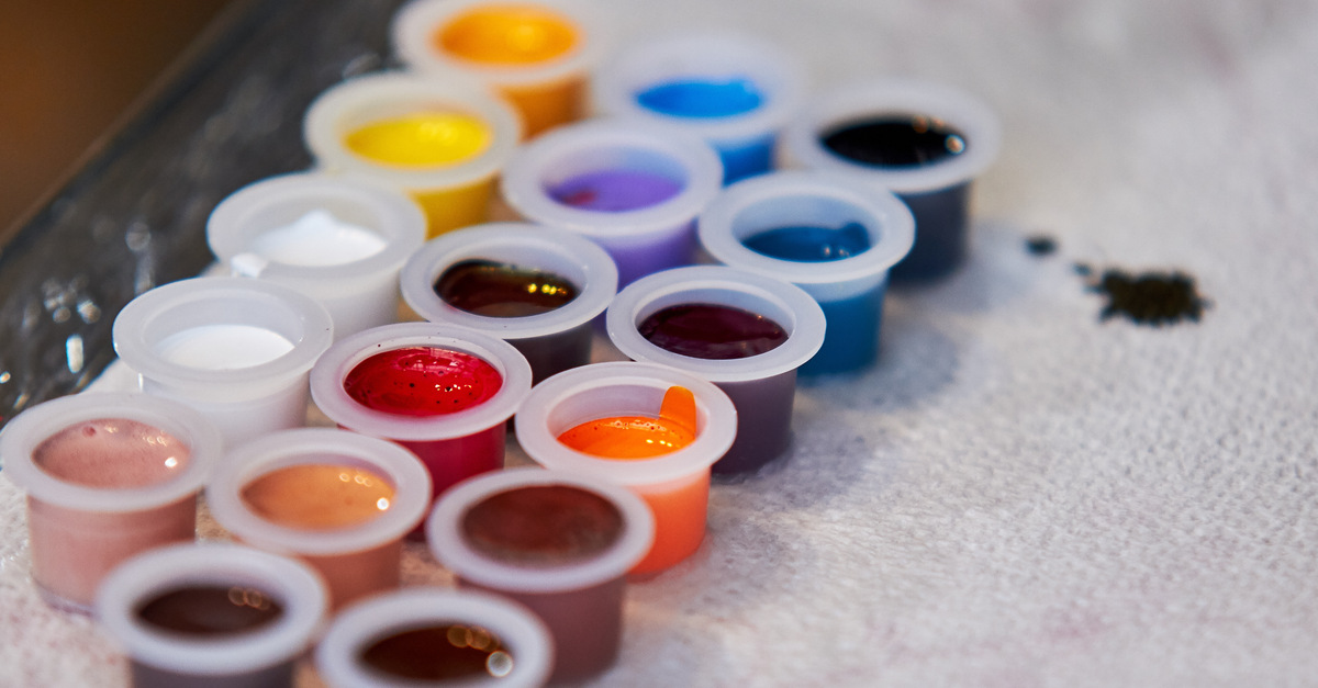 Plastic tattoo ink caps lined in rows on a paper towel. There are different ink colors poured into each cap.